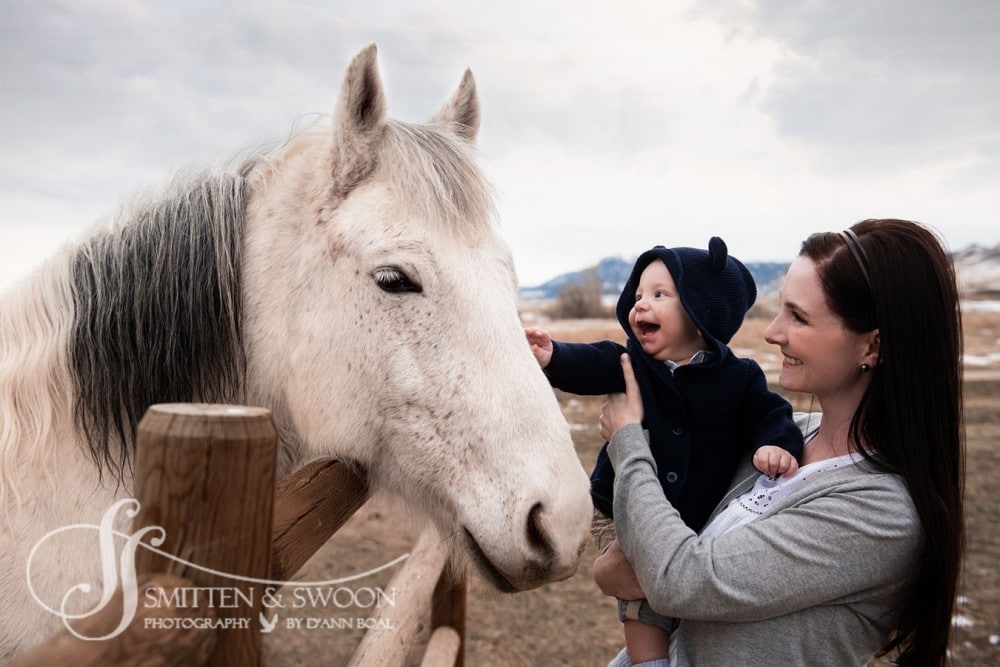 baby boy and mom smiling at white horse