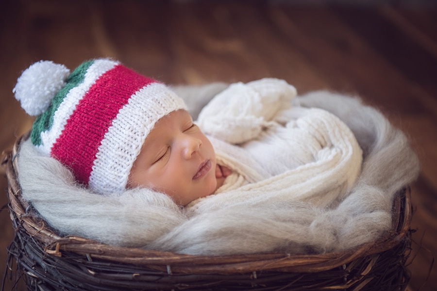 baby boy posed in wooden basket with red and green hat - newborn photographer boulder