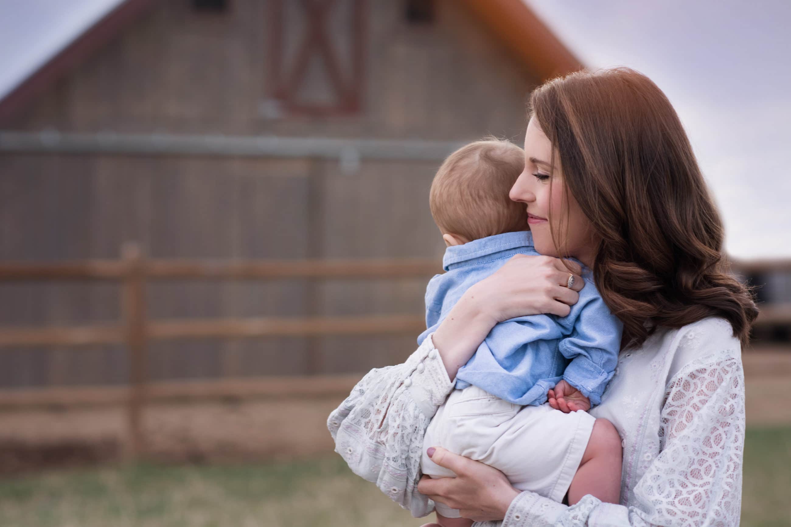 mom and baby boy hugging with rustic barn and fence - boulder photographer