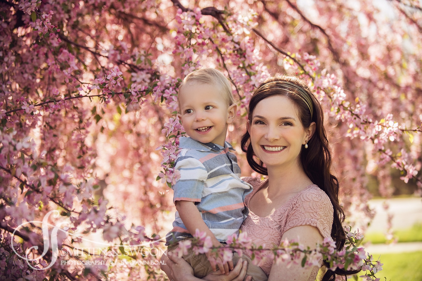 mom and baby boy smiling under pink cherry blossom tree