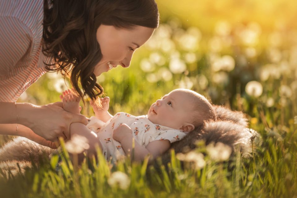 baby laying on grass looking up at her mom and smiling back light flowers - boulder photographer