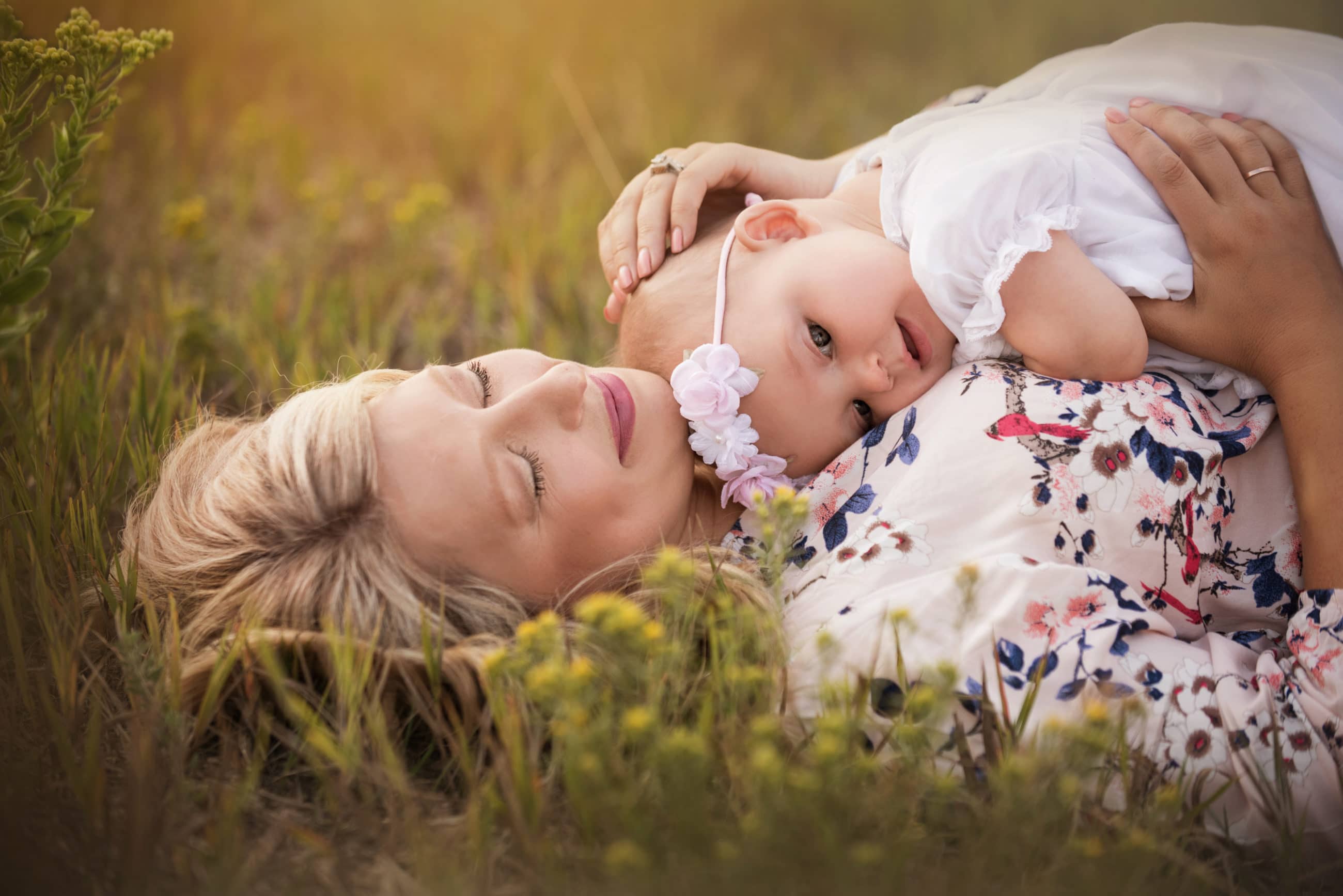 mother holding her baby girl laying on her back in a field of yellow flowers - Denver photographer
