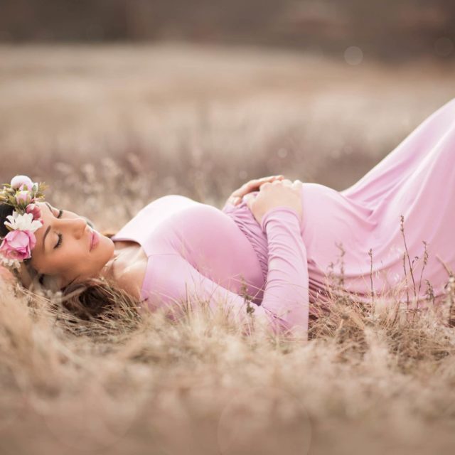 pregnant mother in pink maternity gown and flower crown laying down in golden grass - baby's first year - boulder newborn photographer