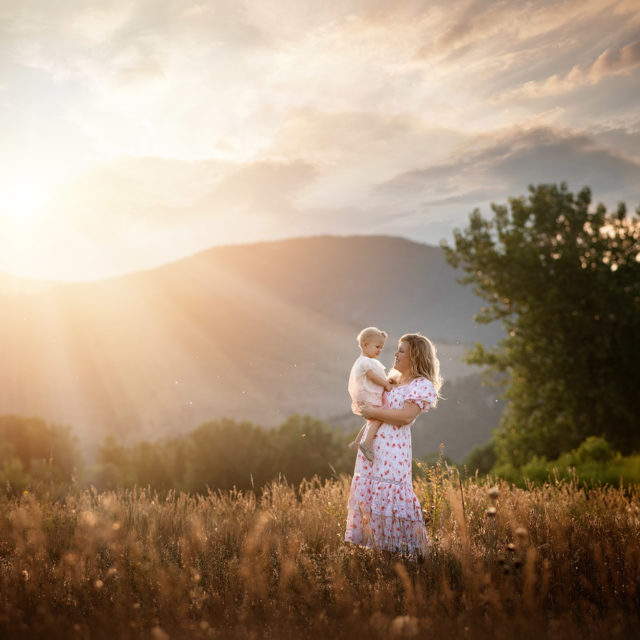 mom holding baby girl in golden light in field of gold with mountains in Colorado Mother daughter photo session | boulder family photographer