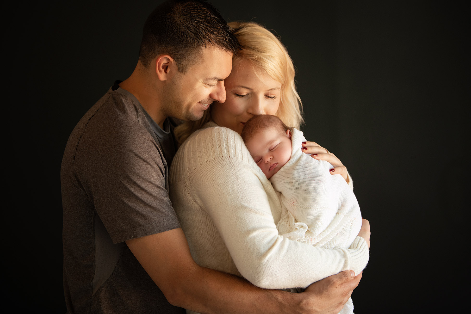 family of three hugging with newborn baby girl in photography studio
